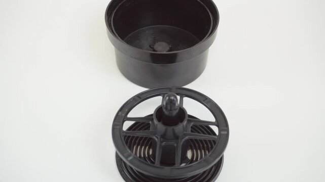 Black film developing tank for 35mm film. Soviet darkroom equipment for manual film processing. Vintage plastic photo tank on white background.