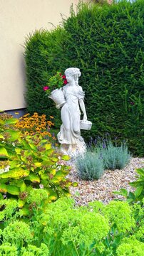 Garden statue holding flowers and surrounded by plants