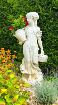 Statue of a woman holding flowers in a garden with colorful plants