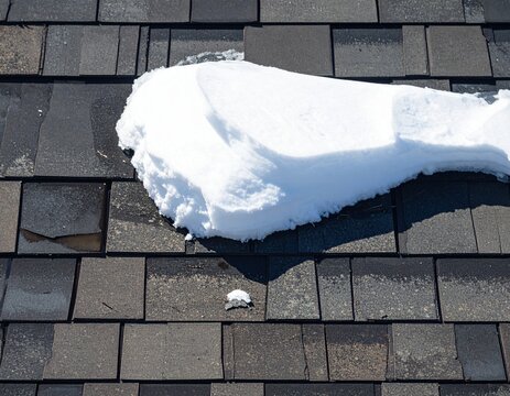 Thick snow layer resting across weathered residential roof shingles