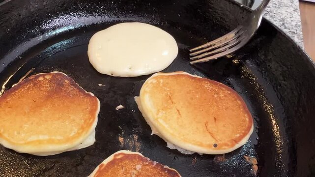 Cooking fluffy homemade pancakes in a hot cast iron skillet, flipping golden brown pancakes with a fork during preparation.