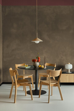 Modern minimalist dining room interior with a round black table, wooden chairs, pendant light, and warm brown wall background in cozy house