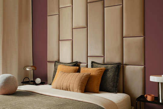 Modern luxury bedroom interior design featuring tall upholstered beige leather headboard wall panel, warm pillows, and ambient lamp lighting