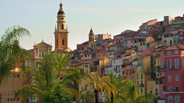 Cinematic view of Menton old town during sunset with palm trees and colorful french riviera buildings.