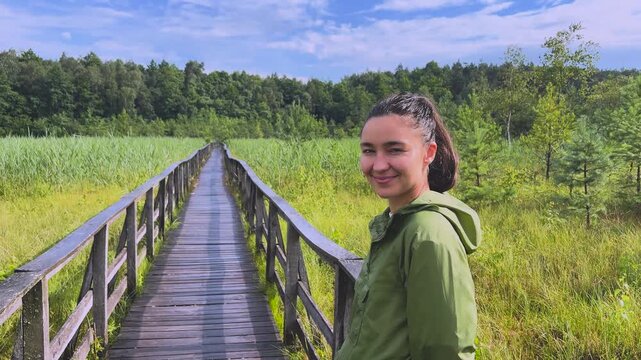 Young woman walking along a wooden boardwalk in a national park turning back and smiling at the camera