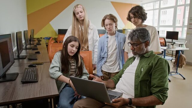 Indian middle aged male teacher explaining coding on laptop to group of teenagers in computer lab ideal for STEM education marketing and school promotional videos