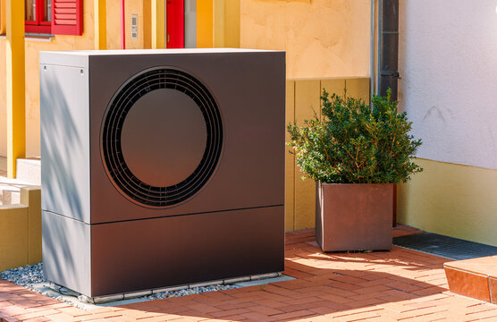 Modern dark air source heat pump outdoor unit installed outside residential house, renewable heating system and green energy concept