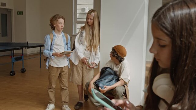 Teenagers talking and using digital devices in school hallway during break. Footage is perfect for educational technology promos and youth lifestyle advertisements