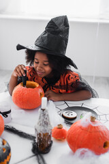 Fototapeta premium Little girl joyfully carves pumpkins in her Halloween costume during a creative autumn celebration