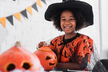 Fototapeta premium Cute little girl joyfully carving pumpkins in her vibrant Halloween costume