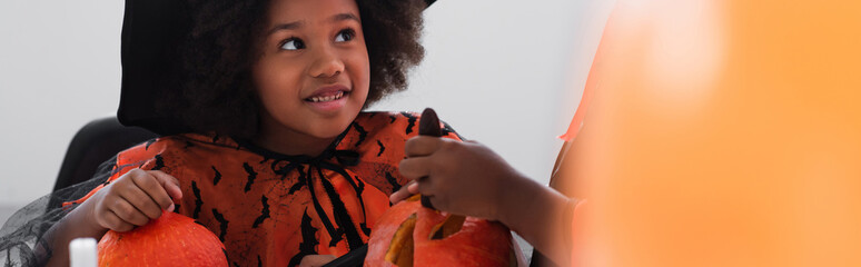 Fototapeta premium Little girl enjoying Halloween fun while preparing pumpkins in her spooky costume
