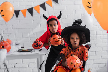 Fototapeta premium Cute siblings celebrating Halloween with vibrant costumes and pumpkins in a cheerful setting