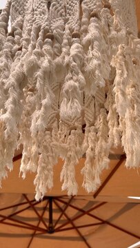 Detailed closeup of cream macrame tassels, knotted cotton fibers and wooden beads creating a warm handmade bohemian decorative texture.
