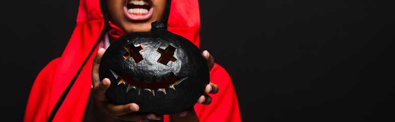 Fototapeta premium Cute little boy in a vibrant Halloween costume holding a spooky pumpkin in excitement