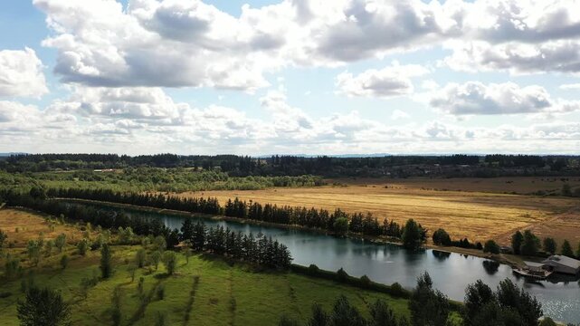 4K aerial drone footage of Warman Lake in Camas, Washington, USA, surrounded by rural homes, green fields and open land, showing waterfront property and countryside under a partly cloudy sky