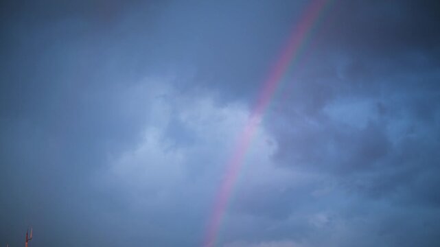 Vibrant rainbow arch appearing in dark stormy sky during overcast weather.