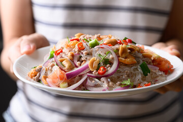 Thai spicy glass noodle salad with minced pork and shrimp (Yum Woon Sen) on a white plate holding by woman hand © nungning20