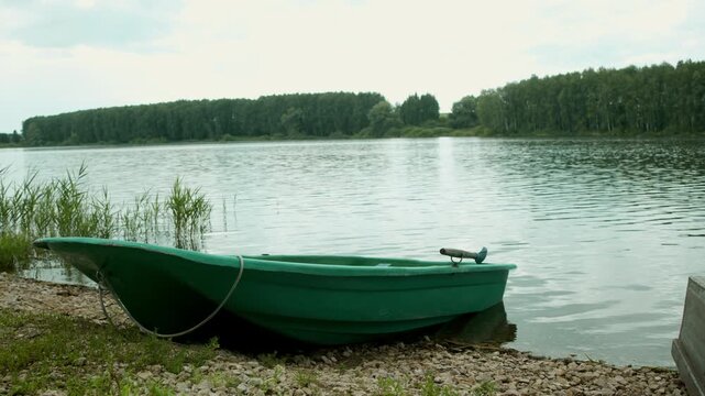 Green rowboat rests on rocky shore beside calm forest lake. Peaceful summer landscape invites boating and outdoor recreation.