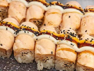 Close-up view of neatly arranged seared sushi rolls drizzled with sauce and black sesame seeds © Robert