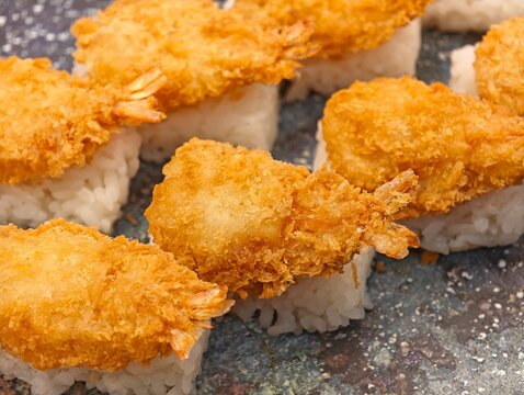 Close-up golden crispy ebi tempura nigiri sushi arranged on a dark stone plate