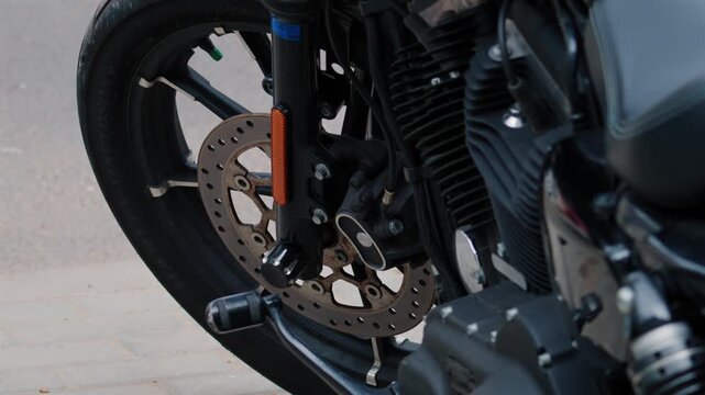 Close up shot of black motorcycle front wheel parked on city street side.
