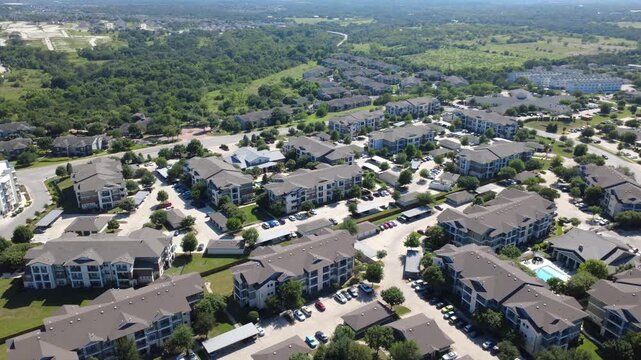 Vast garden apartment complexes spread toward Onion Creek greenbelt. Tidy carport bays, multi level buildings, lush tree lines highlight sustained residential community expansion, Austin, Texas
