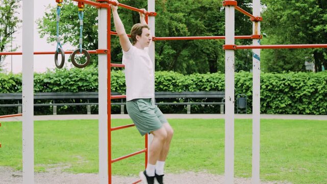 Fit young man doing a hanging core and abs workout at an outdoor gym. He performs leg raises on a pullup bar, practicing calisthenics for fitness and health. High quality 4k footage