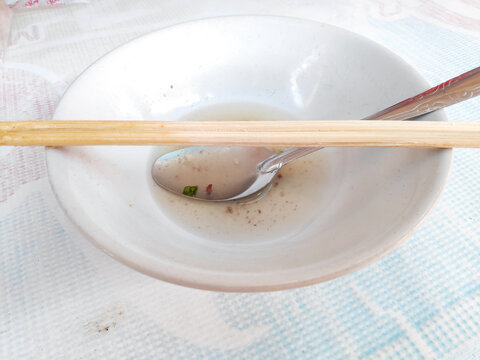 Detail view of a used white ceramic bowl with a spoon and chopsticks after eating soup