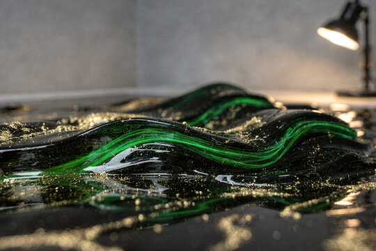 Abstract flowing black and emerald green glossy wave with golden glitter dust under soft desk lamp lighting