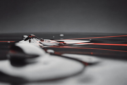 Abstract macro shot of liquid ripples and drops reflecting vibrant red laser light against a dark surface
