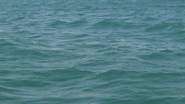 Calm ocean surface with natural wave texture. Transparent water of deep blue-green hue. Sea water texture with small waves. Minimalistic background with ocean waves. Sea surface