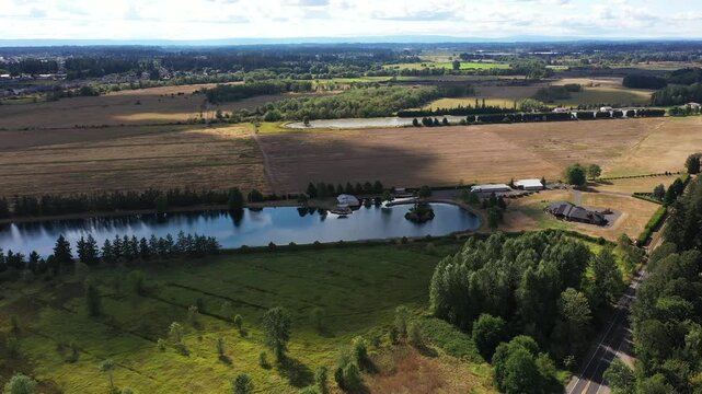 4K aerial drone footage of Warman Lake in Camas, Washington, USA, surrounded by rural homes, green fields and open land, showing waterfront property and countryside under a partly cloudy sky