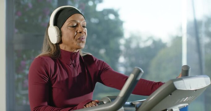 African American woman in maroon top glancing at console tapping control changing pace by window