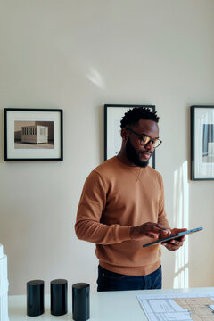 Vertical shot of young adult Black man using tablet while reviewing floor plan, supporting architecture workflow and digital planning. Ideal for real estate, design tech, project management