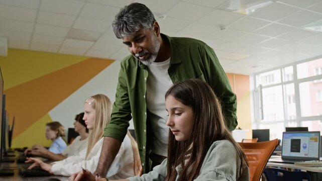 Indian middle aged teacher guiding Caucasian teenager student typing on keyboard in computer class. Clip is perfect for promoting STEM education, coding bootcamps, and modern school learning