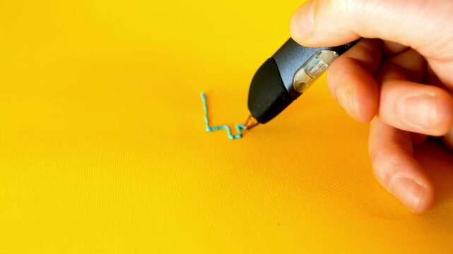 Bitcoin creation man hand draws cryptocurrency symbol with 3d printer pen on yellow background in 4K Ultra HD footage.
