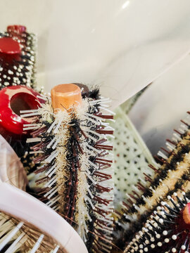 Group of used hairbrushes featuring round blow drying tools and red paddle brushes in container