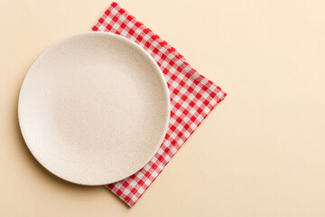 Fototapeta premium Top view on colored background empty round white plate on tablecloth for food. Empty dish on napkin with space for your design