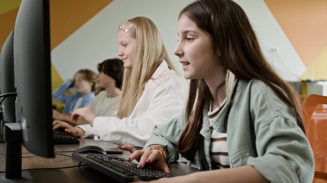 Caucasian teenage girls learning coding in computer science class, typing on keyboards as camera panning. Ideal for promoting STEM education and modern school curriculum