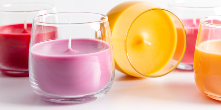 Colorful Scented Soya Wax Candles in Glass Jars on White Background Close Up. Cozy Autumn Home Decor, Aromatherapy and Spa Concept with Purple, Red, Yellow and Pink Paraffin Candles