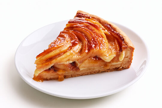 Part de tarte aux pommes sur fond blanc, sur assiette blanche. P&acirc;te bris&eacute;e, tranches de pommes caram&eacute;lis&eacute;es avec leur jus et migaine fa&ccedil;on cr&egrave;me p&acirc;tissi&egrave;re