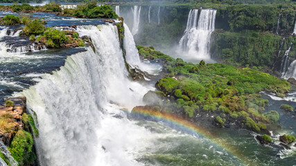 Fototapeta premium Iconic Iguazu Falls with a prominent rainbow over the churning water, captured in high resolution to highlight the mist, vegetation, and dramatic scale 