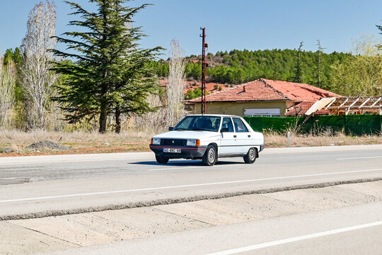 A white 1980s Renault 9 Spring Broadway classic sedan drives down a country road against a rural backdrop in Anatolia; a classic OYAK cult car on the roads of Konya Province, Turkey