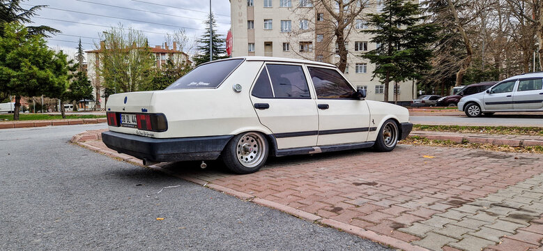 A cream-white, tuned Tofas Sahin classic car with a lowered suspension and chrome rims is parked on a residential street in Konya; a tuned Turkish sedan classic from the 1990s in Turkey 02.04.2025