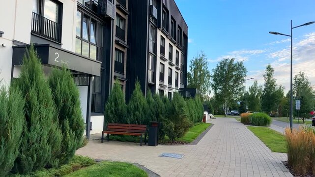 Modern pedestrian walkway with paving slabs and multi-level landscaping on street near condominium. Juniper trees in landscape design. Multifamily housing. Street at contemporary residential multifami