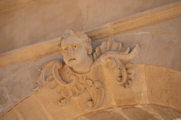 Modica, Italy  1st August 2026: Baroque architectural detail with carved grotesque face and ornate stonework on a balcony in Sicily. © Leckerstudio