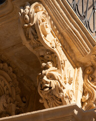 Modica, Italy  1st August 2026: Baroque architectural detail with carved grotesque face and ornate stonework on a balcony in Sicily. © Leckerstudio