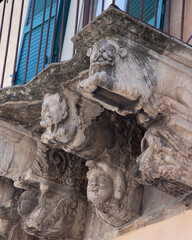Modica, Italy  1st August 2026: Baroque architectural detail with carved grotesque face and ornate stonework on a balcony in Sicily. © Leckerstudio