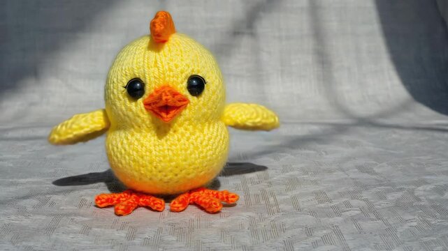 A handcrafted, vibrant yellow crocheted chick with orange feet and a beak, sitting on a surface.