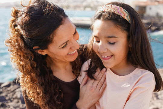 Happy latin mother having tender moment with little daughter on the beach - Summer vacation, family love and mom day concept